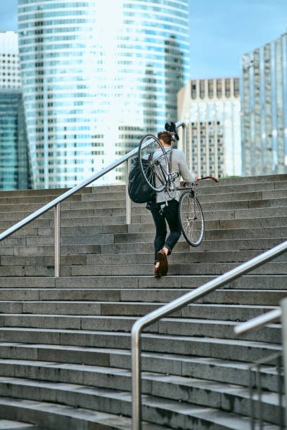 Shot of a young businessman carrying his bicycle while walking up steps in a city