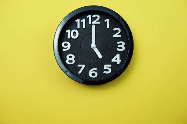 istock Black round clock showing five o'clock on yellow background 1167696843
