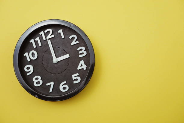 istock Black round clock showing eleven o'clock on yellow background 1167697680