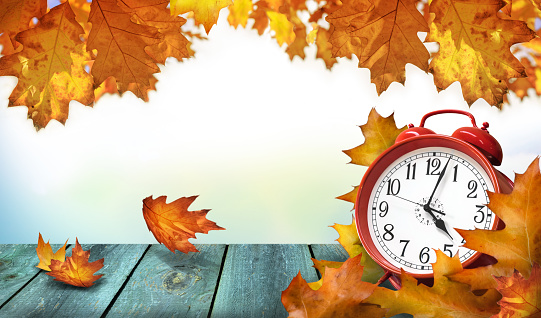 Clock and autumn leaves on the wooden table - daylight saving time concept