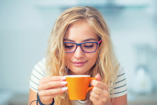 Cup of coffee in hand of happy young woman. Attractive girl drinking morning tea.