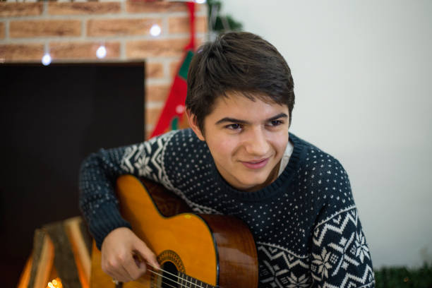 retrato de joven tocando su guitarra y cantando en el interior cerca del árbol de navidad - suit jeans men musician fotografías e imágenes de stock