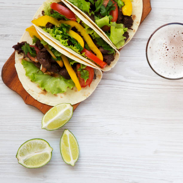 Beef tacos with salad, tomato and beer on a white wooden background, top view. Copy space. From above.