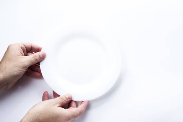 istock Man two hands hold a white plate on white background and top view. Hunger concept. Empty copy space 1167710627