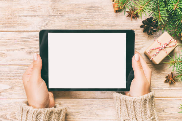 istock woman hands using tablet computer on wooden table bachground. cristmas shopping time. Happy Christmas mock up background, top view. Toned 1167716831
