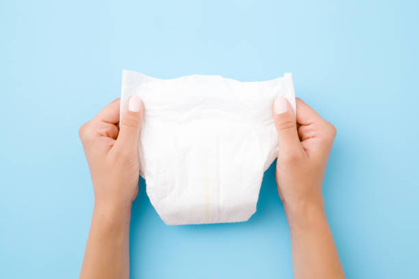 Woman hands holding white baby diaper on pastel blue background. Closeup. Top view. Woman hands holding white baby diaper on pastel blue background. Closeup. Top view. adult diaper stock pictures, royalty-free photos & images