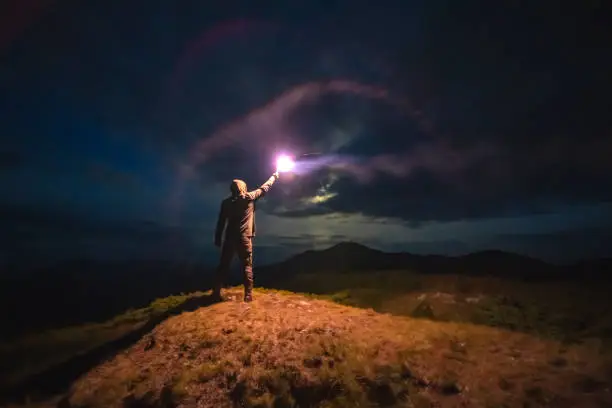 Photo of The man with a bright firework stick standing on a mountain. evening night time