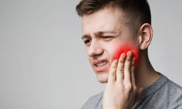 homem novo frustrante que toca em seu dente e na face sobrancelhas franzidas - dor de dente - fotografias e filmes do acervo