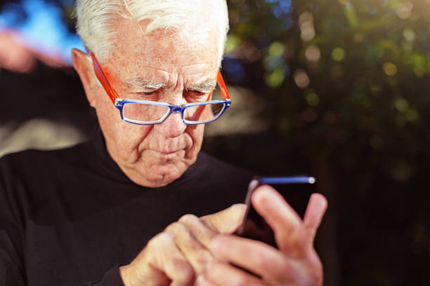 Senior man squints at his mobile phone, sending a text
