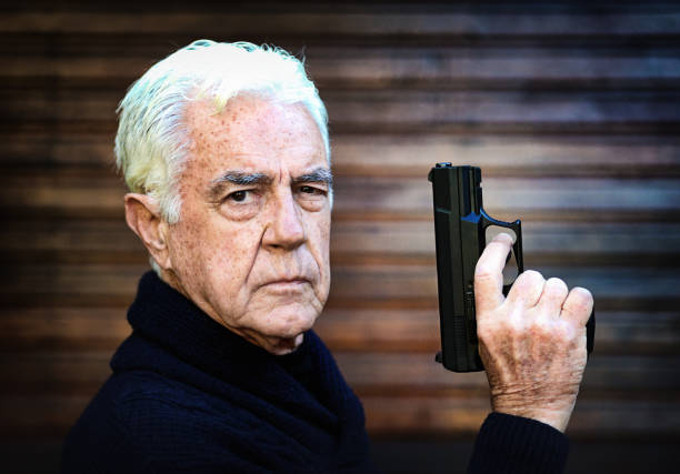 shallow depth of focus action portrait of serious and attractive hitman or special agent man holding gun pointing the handgun to the camera isolated on dark background in Hollywood style movie