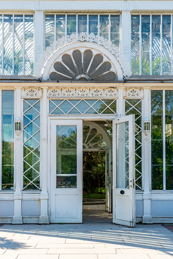 Outdoor facade front view of an old white ornamented glass greenhouse entrance with open door. Gothenburg Sweden vertical composition.