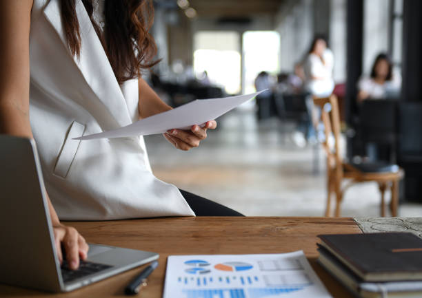 istock Female executive hold the data graph in hand and are using a laptop. She sat on the desk in office. 1167729620