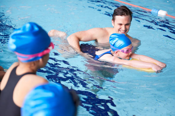 entrenador masculino en el agua dando grupo de niños clase de natación en piscina cubierta - floating on water swimming pool men water fotografías e imágenes de stock