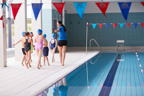 тренер-женщина гуляет с детьми в классе плавания по краю крытого бассейна - swimming child swimming pool indoors стоковые фото и изображения