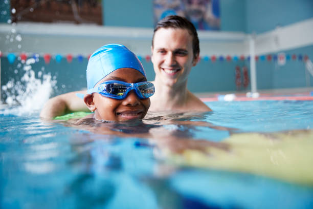entrenador de natación masculino dando niño sosteniendo flotador de una a una lección en la piscina - child swimming pool swimming little boys fotografías e imágenes de stock