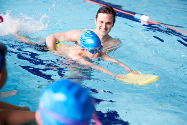 entrenador masculino en el agua dando grupo de niños clase de natación en piscina cubierta - floating on water swimming pool men water fotografías e imágenes de stock