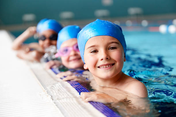 Portrait Of Children In Water At Edge Of Pool Waiting For Swimming Lesson Portrait Of Children In Water At Edge Of Pool Waiting For Swimming Lesson swimming cap stock pictures, royalty-free photos & images