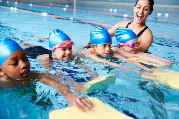 weibliche trainerin in wasser geben gruppe von kindern schwimmstunde im hallenbad - schwimmen fotos stock-fotos und bilder