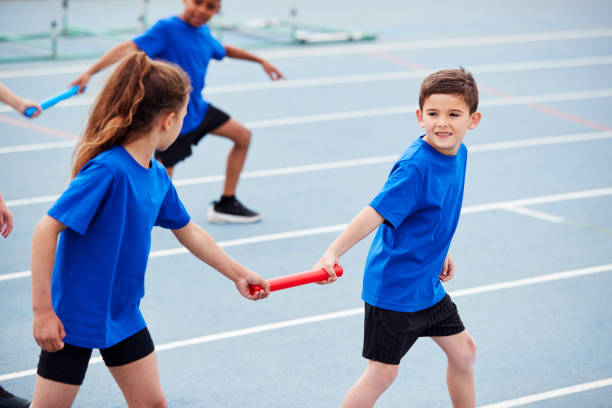 les enfants dans l'équipe d'athlétisme concourant dans la course de relais le jour de sports - course de relais photos et images de collection