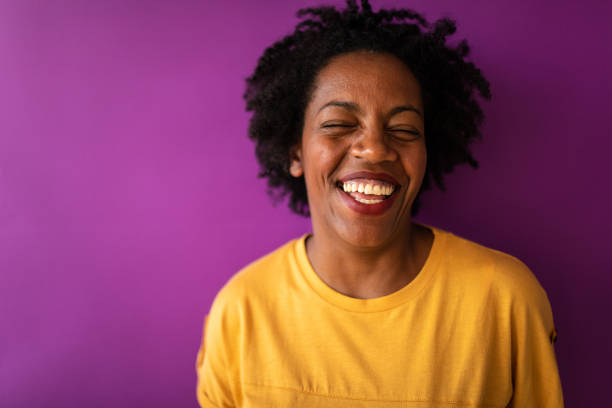 Confident Black woman standing in front of purple wall laughing and looking at camera