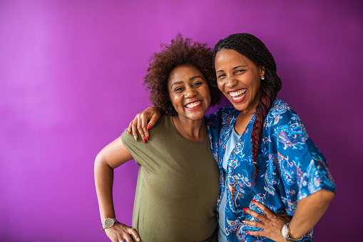 Portrait of two best female friends embracing in front of purple wall, and smiling happily