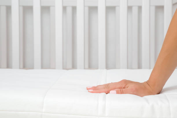 흰색 매트리스에 눌러 여자 손. 아기 침대의 경도 와 부드러움을 검사 하는 어머니. 최고의 유형과 품질의 선택. 측면 뷰. 닫아. - baby duvet sleeping bed 뉴스 사진 이미지