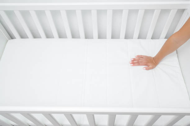 mujer presionando a mano sobre el colchón blanco. madre comprobando la dureza y suavidad de la cama de bebé. elección del mejor tipo y calidad. vista de arriba hacia abajo. de cerca. - cot fotografías e imágenes de stock