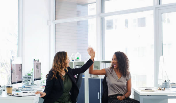 When you work together, you win together Shot of two young businesswomen giving each other a high five in a modern office high five stock pictures, royalty-free photos & images