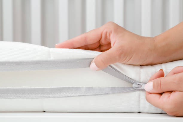 Woman's hand opening cover of new white mattress with zipper. Mother checking hardness and softness of baby bed. Choice of the best type and quality. Closeup. Woman's hand opening cover of new white mattress with zipper. Mother checking hardness and softness of baby bed. Choice of the best type and quality. Closeup. upholstered furniture stock pictures, royalty-free photos & images