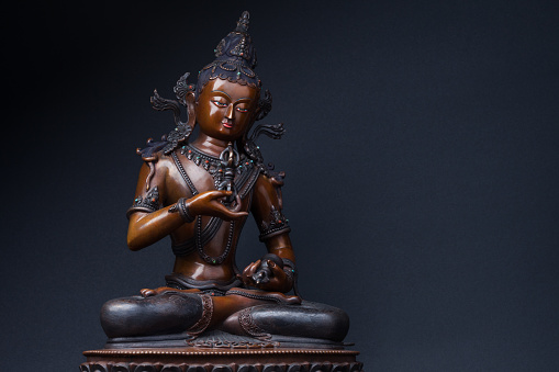 Vajrasattva's sculpture sitting with a dorje in one hand and a hand bell in another, on black background. Vajrasattva - a secret form of Buddha Samantabhadra.