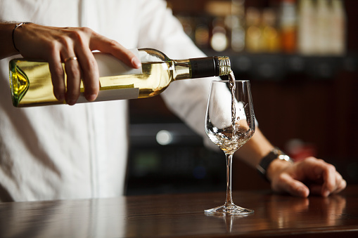 Male sommelier pouring white wine into long-stemmed wineglasses.