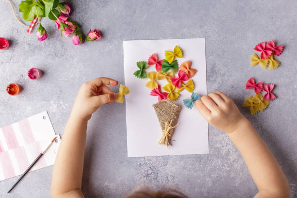 papierowe rzemiosło na dzień matki, 8 marca lub urodziny. małe dziecko robi bukiet kwiatów z kolorowego papieru i kolorowego makaronu - flower spring bouquet child zdjęcia i obrazy z banku zdjęć