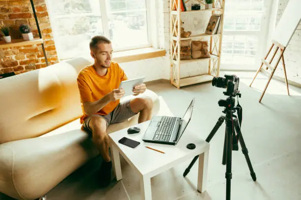 Photo of Caucasian male blogger with camera recording video review of gadgets at home