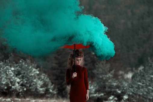 Woman wearing red dress, holding an umbrella surrounded by smoke