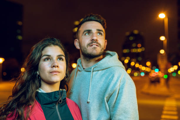 Man and young woman looking up with hope in downtown Barcelona at night stock photo