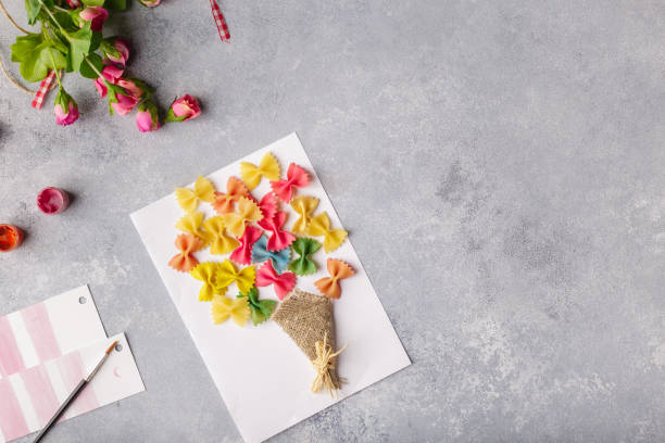 Paper crafts for mother day, 8 march or birthday. Small child doing a bouquet of flowers out of colored paper and colored pasta stock photo