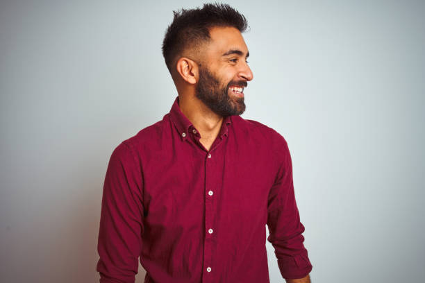 istock Young indian man wearing red elegant shirt standing over isolated grey background looking away to side with smile on face, natural expression. Laughing confident. 1167769083