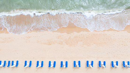 Aerial top view on the sandy beach. Umbrellas, sand, beach chairs and sea waves.