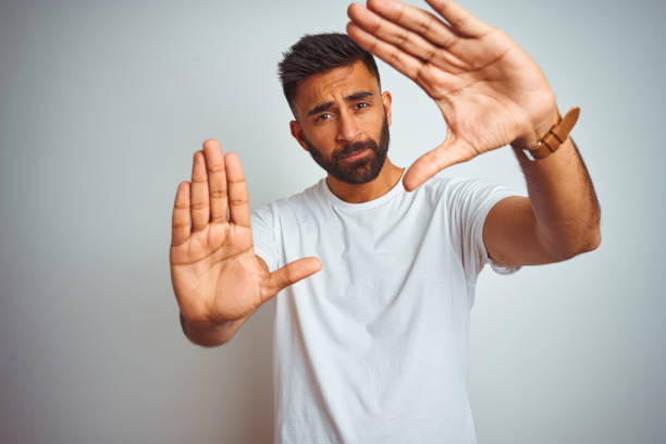 istock Young indian man wearing t-shirt standing over isolated white background doing frame using hands palms and fingers, camera perspective 1167770584