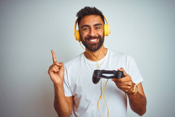 istock Arab indian gamer man playing video game using headphones over isolated white background very happy pointing with hand and finger to the side 1167770621
