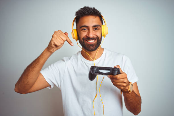 istock Arab indian gamer man playing video game using headphones over isolated white background very happy pointing with hand and finger 1167770636
