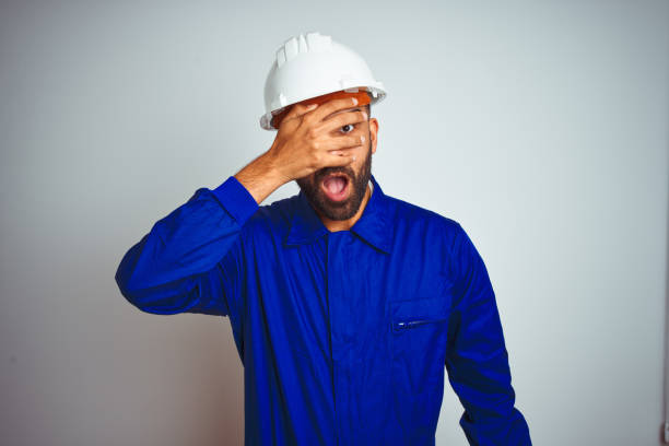 istock Handsome indian worker man wearing uniform and helmet over isolated white background peeking in shock covering face and eyes with hand, looking through fingers with embarrassed expression. 1167770780