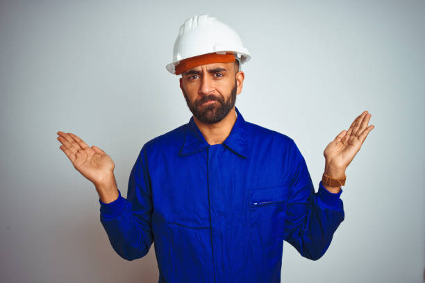 istock Handsome indian worker man wearing uniform and helmet over isolated white background clueless and confused expression with arms and hands raised. Doubt concept. 1167770783