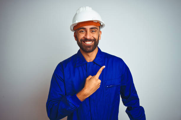 istock Handsome indian worker man wearing uniform and helmet over isolated white background cheerful with a smile of face pointing with hand and finger up to the side with happy and natural expression on face 1167770794