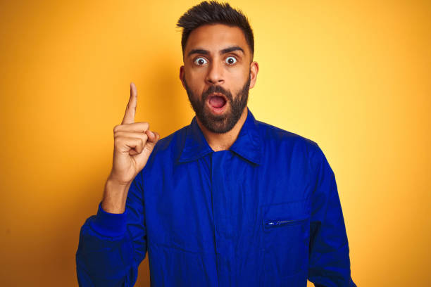 istock Handsome indian worker man wearing uniform over isolated yellow background pointing finger up with successful idea. Exited and happy. Number one. 1167770840