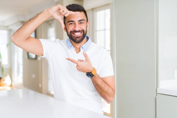 istock Handsome hispanic man casual white t-shirt at home smiling making frame with hands and fingers with happy face. Creativity and photography concept. 1167773992