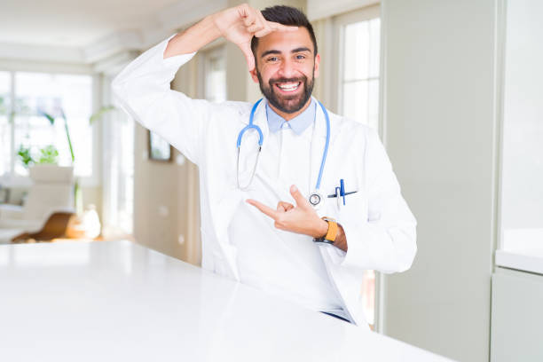 istock Handsome hispanic doctor man wearing stethoscope at the clinic smiling making frame with hands and fingers with happy face. Creativity and photography concept. 1167774140