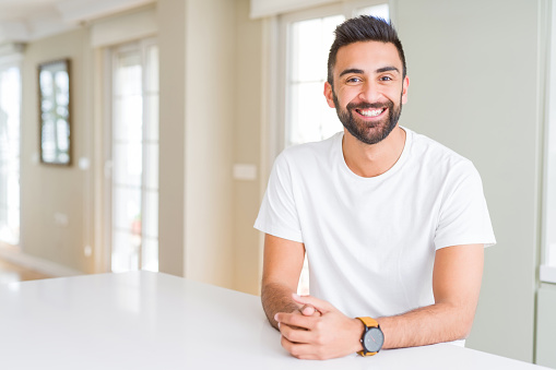 Handsome hispanic man casual white t-shirt at home with a happy and cool smile on face. Lucky person.