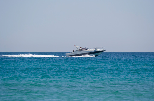 A man races a jet ski at top speed in the Mediterranean Sea, standing up in the jet ski.