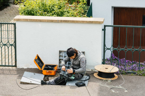 Paris, France - May 20, 2019: Horizontal view from above of engineer worker arranging setting optic fiber in the manhole during local deployment of high speed internet